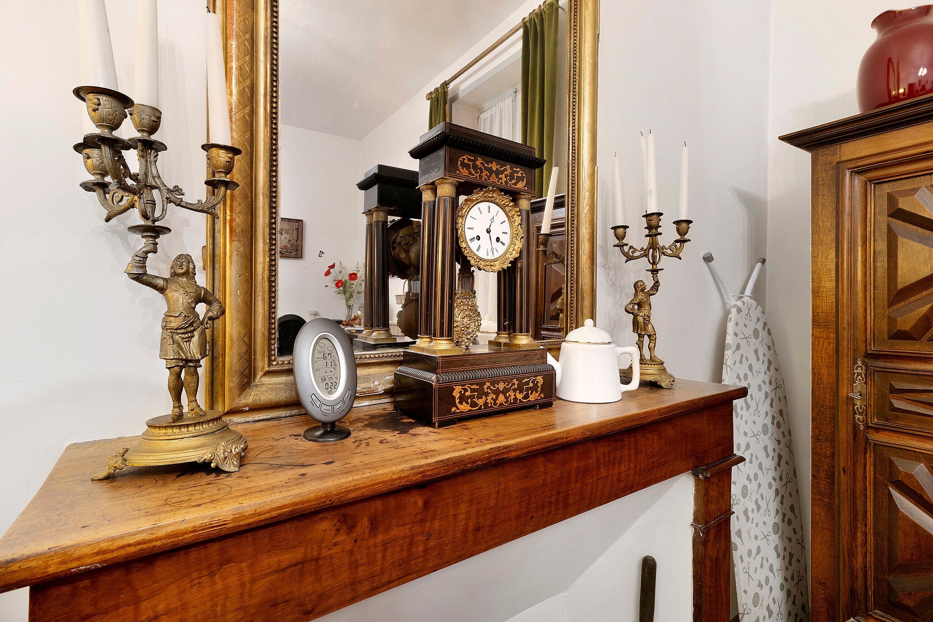 Un aparador de madera con un reloj, un candelabro y un florero.