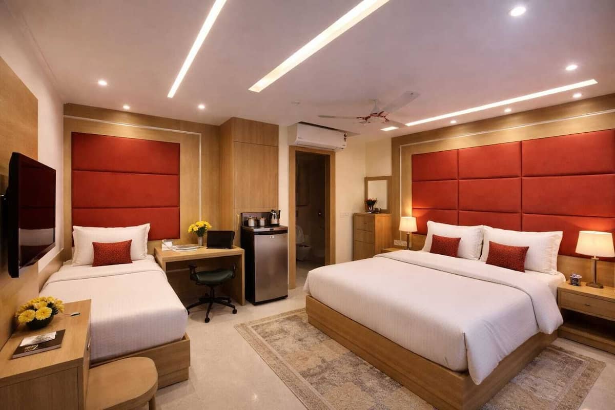 A hotel room with two beds, a desk, a refrigerator, and a television.