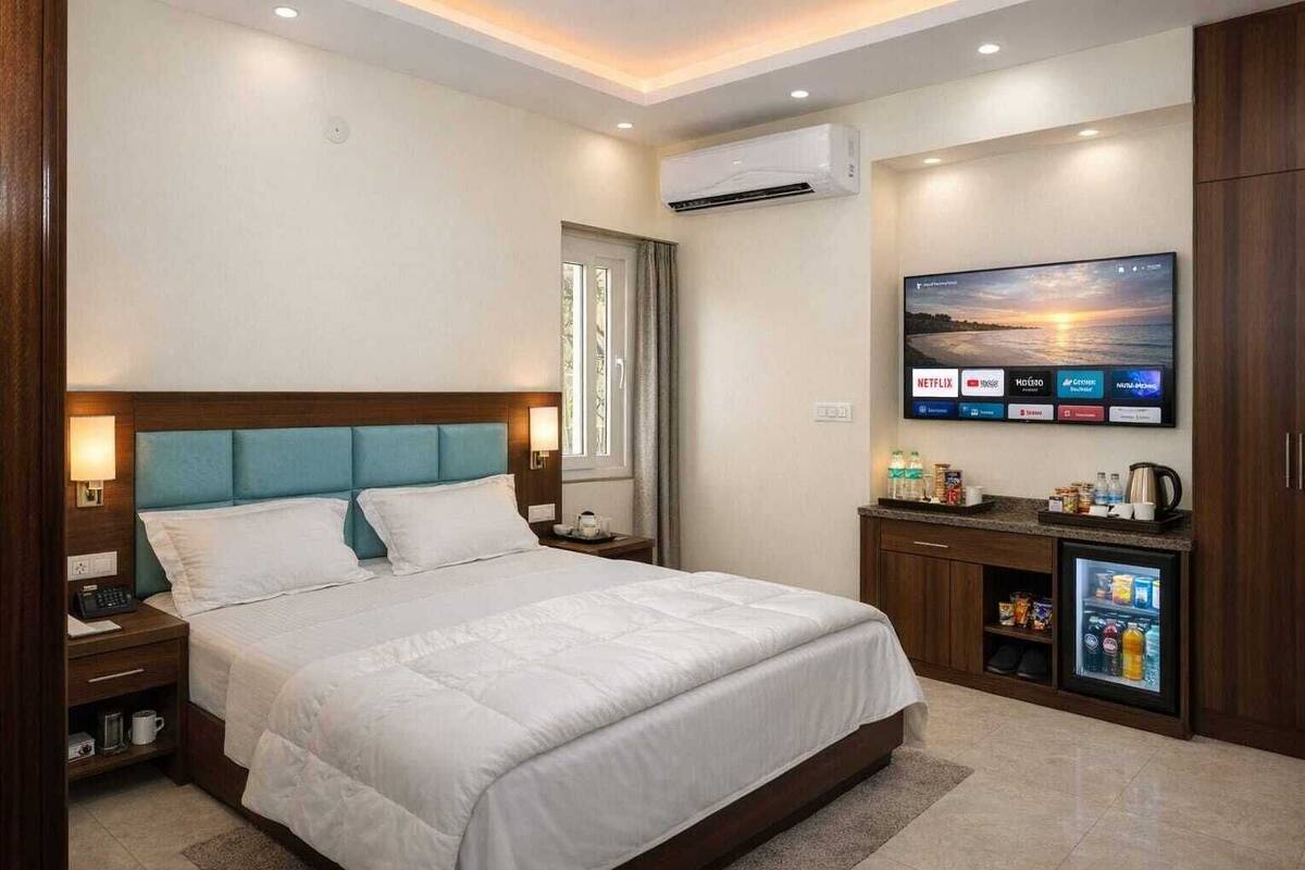 A hotel room with a bed, bedside tables, a TV, an air conditioner, and a minibar.
