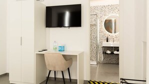 A room with a white desk, a chair, a flat-screen TV, a wardrobe, a bathroom with a sink and a mirror. - Flamingo affittacamere - Camera 4 (Matera)