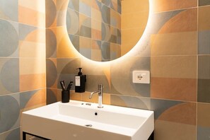 A bathroom with a white sink, a mirror, and a wall with a geometric tile pattern. - Flamingo affittacamere - Camera 1 (Matera)