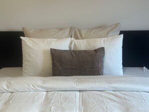 Un lit avec une literie blanche et un oreiller marron foncé.