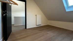 Une pièce vide avec un plafond en pente, un radiateur et une porte sur laquelle est fixé un porte-manteau.