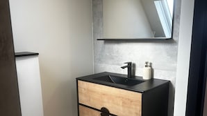 Une salle de bain moderne comprenant des toilettes, un lavabo avec un plan de travail noir, un meuble à tiroirs en bois et un miroir au-dessus du lavabo.