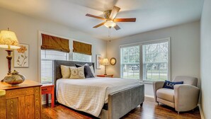 A bedroom with a bed, a chair, a nightstand, a lamp, a ceiling fan, and large windows. - Family + Pet Friendly: Fort Worth Home Near TCU! (Fort Worth)