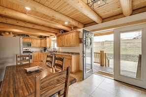 Un interior de madera con una mesa de comedor, sillas, armarios y un ventanal corredero que da a un espacio exterior.