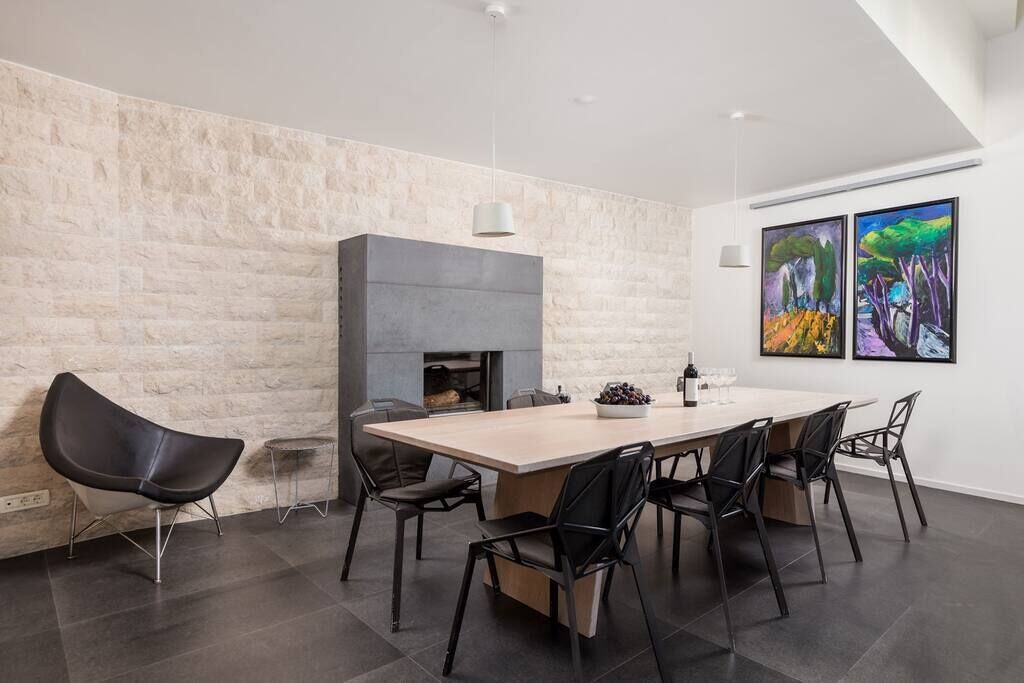 Un espace repas moderne avec une grande table, des chaises noires, un mur décoratif en pierre et deux tableaux.