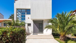 Una moderna casa a due piani con un'ampia finestra al piano terra e un portone con pannello vetrato.