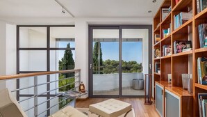 Un ampio balcone con una porta vetrata che dà su una terrazza, un divano in pelle e una libreria in legno piena di libri.