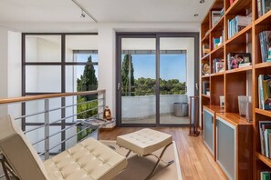 Ein geräumiger Balkon mit Glastür zum Terrassenbereich, ein Ledersofa und ein Bücherregal voller Bücher.