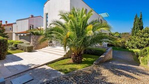 Una casa moderna con facciata bianca, vialetto lastricato e una palma nel giardino.