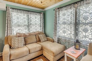 Un salon avec un canapé beige, des coussins à motifs, une petite table sur laquelle est posée une lanterne, et des rideaux à motifs.