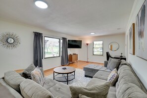 A modern living room with a grey sofa, a round coffee table, and a flat-screen TV mounted on the wall. - Quiet Downtown Cary Home w/ Screened Porch (Cary)