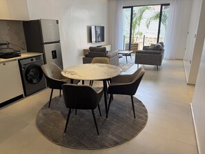 A modern kitchen with a washing machine, a dining area with a marble table, and a living space with sofas and a TV. - Omica 1 Residence (Kigali)
