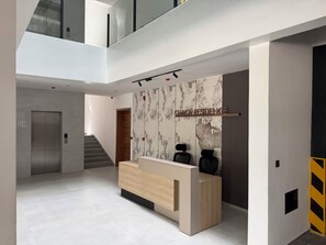 A modern reception desk with a marble wall backdrop, a staircase, and a visible elevator. - Omica 1 Residence (Kigali)
