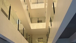 Een modern interieur met een open centrale ruimte, glazen balustrades en een zichtbare lift.