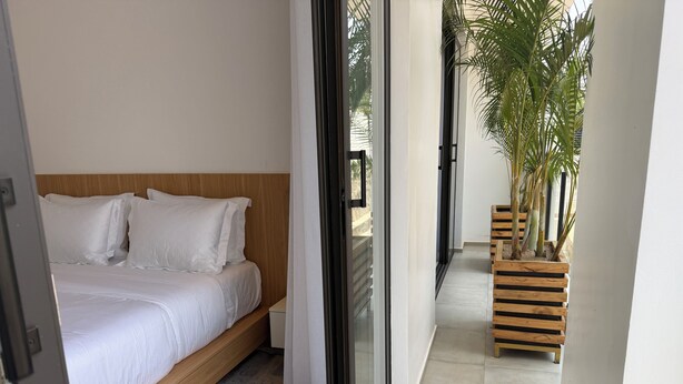 Een slaapkamer met een bed, een houten hoofdbord, een grijs tapijt en uitzicht op een balkon met planten.