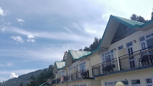 A multi-story hotel with balconies, a staircase leading to the entrance, and a mountainous backdrop. - Kufri Paradise Villa By Mountain Bee (Theog)