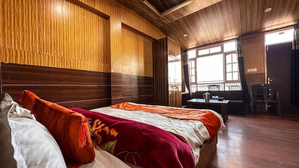 A room with a wooden ceiling, a bed with multiple pillows, a small table, and a chair. - Kufri Paradise Villa By Mountain Bee (Theog)