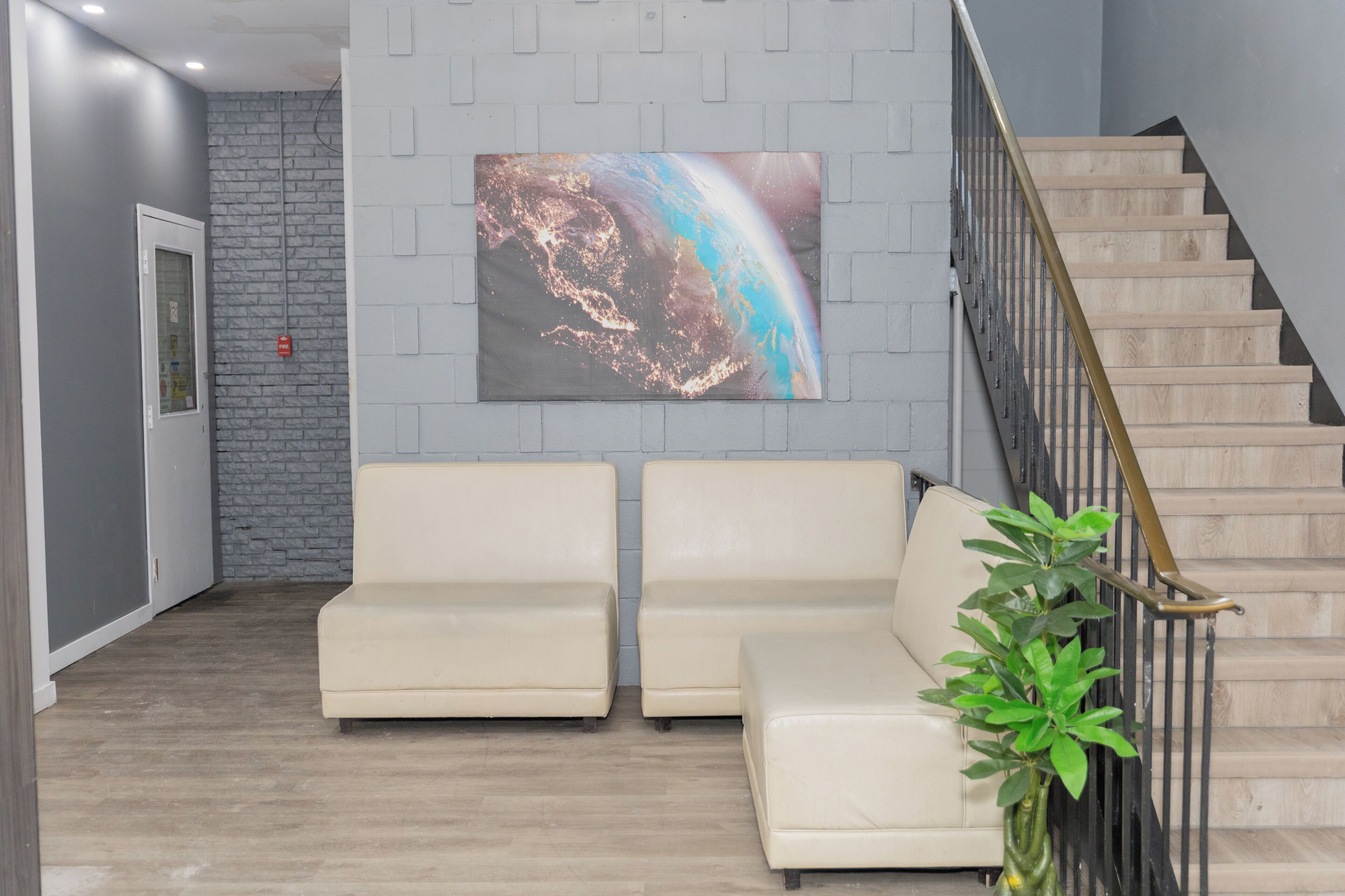 A reception area with a staircase, two sofas, a plant, and a large abstract painting on the wall.
