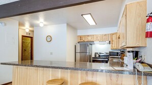 A kitchen with wooden cabinets, a stainless steel refrigerator, a microwave, and a coffee maker. There are three wooden stools at the counter. - Condo 3 Mi to Winter Park Resort: Community Perks! (Winter Park)