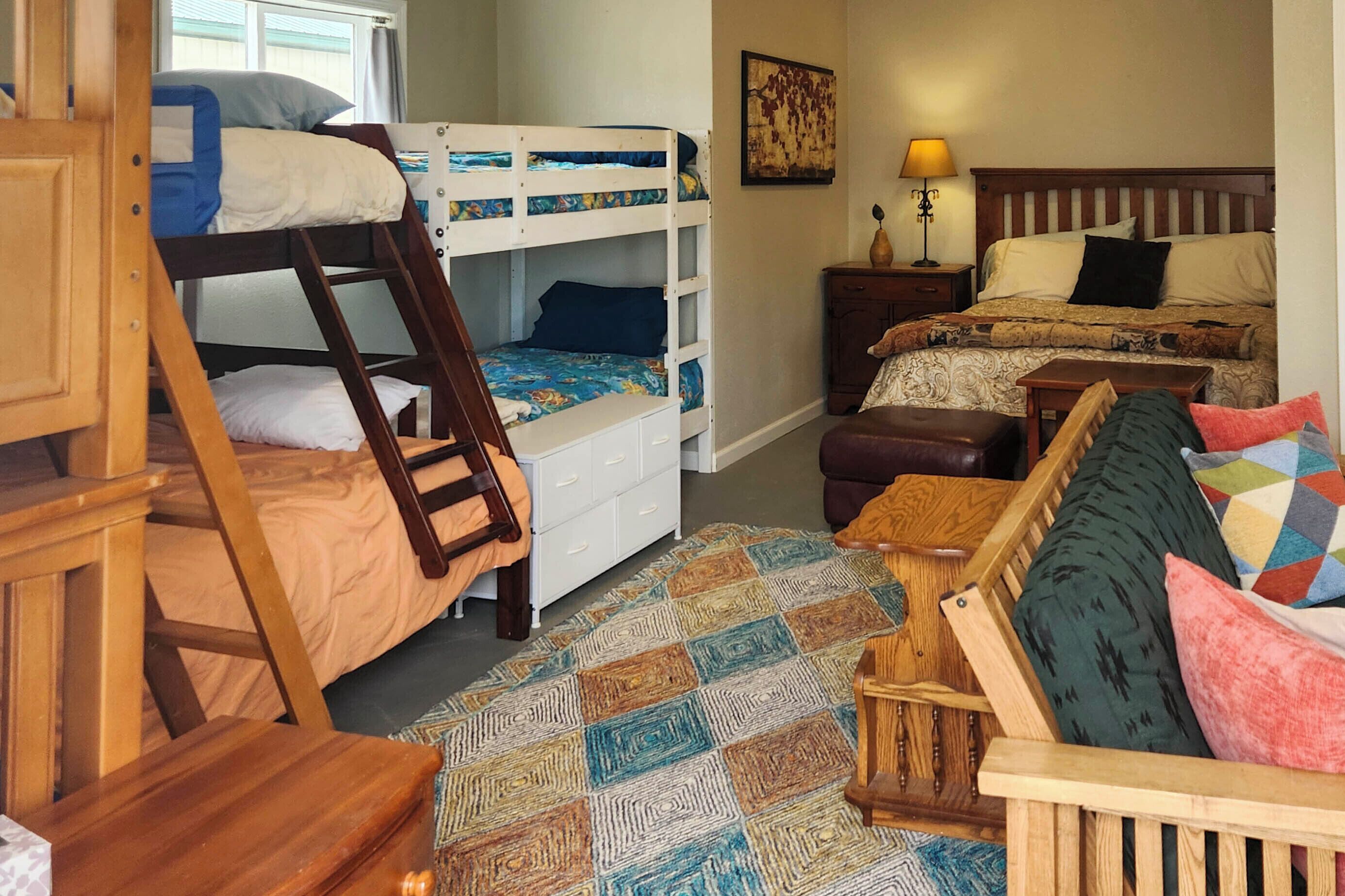 A room with bunk beds, a desk, a chair, a patterned rug, and a nightstand with a lamp.
