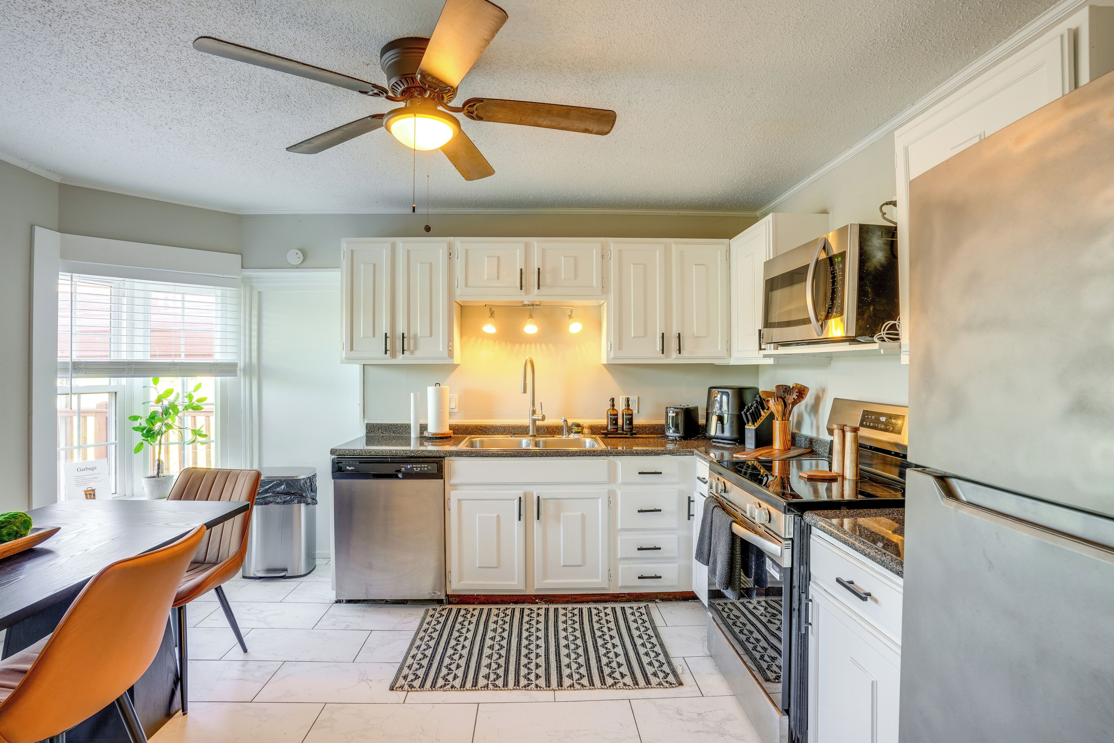A modern kitchen with white cabinets, a ceiling fan, stainless steel appliances, and a dining area with a table and chairs.
