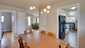 A dining area with a wooden table and chairs, a modern chandelier, and a kitchen with a refrigerator. - Deck & Patio! Walkable Downtown Cary Home (Cary)
