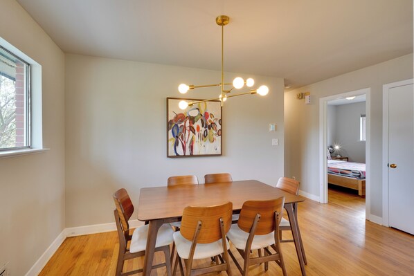 A dining area with a wooden table and chairs, a modern chandelier, and a colorful abstract painting on the wall. - Deck & Patio! Walkable Downtown Cary Home (Cary)