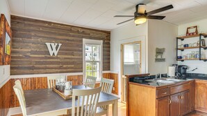 Zona pranzo con parete in legno, ventilatore a soffitto e cucina con mobili in legno e piano di lavoro nero.