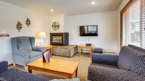 A living room with a sofa, armchair, coffee table, fireplace, television, and decorative wall art. - Mtn Base w/ Hot Tub Access Near Winter Park Resort (Winter Park)