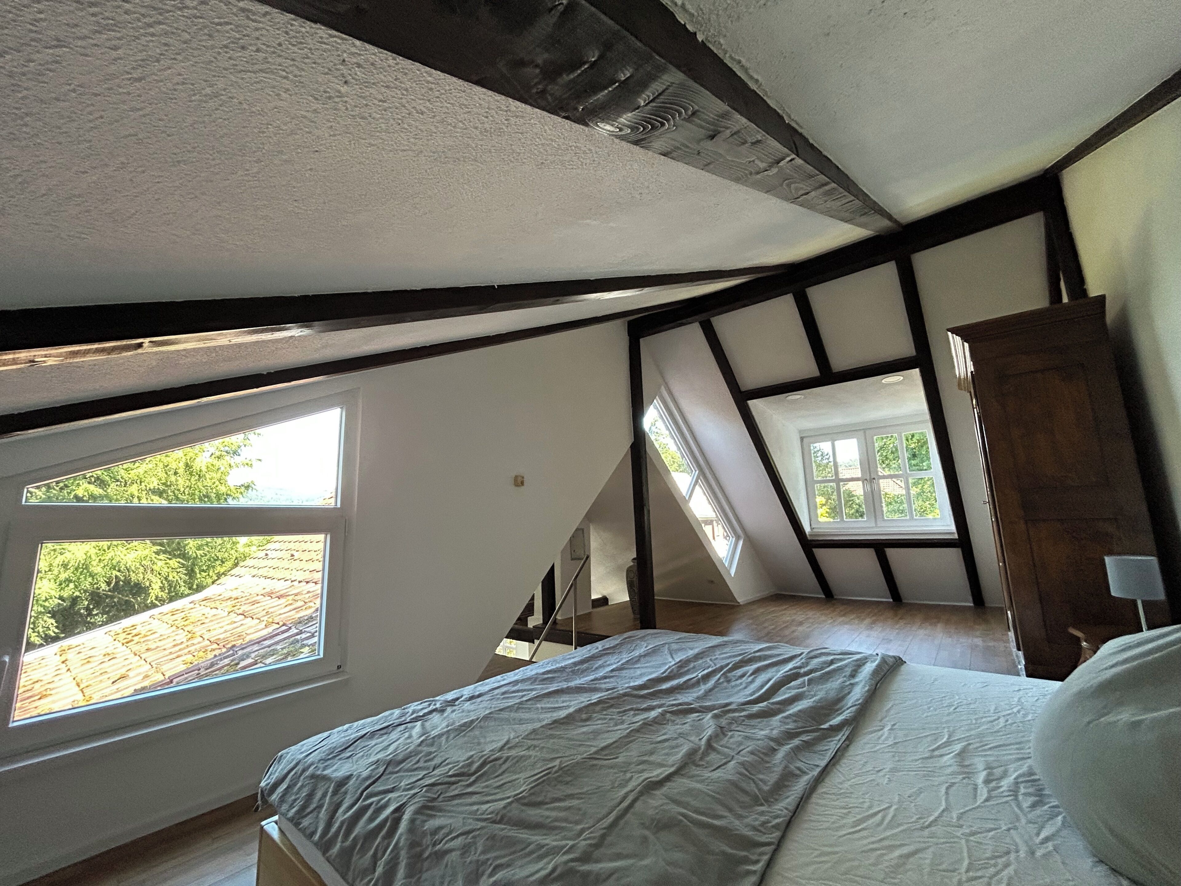 Een slaapkamer met een schuine plafond, dakramen, een bed en een houten garderobe.