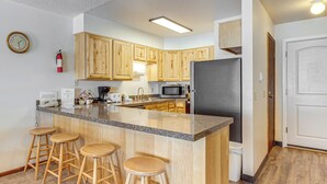 A kitchen with wooden cabinets, a granite countertop, a refrigerator, a microwave, a sink, and three stools. - Walk to Hideaway Park! All-Season Winter Park Gem (Winter Park)