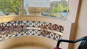 A balcony with a metal railing, a red cushioned chair, and a view of a building with a tiled facade. - The Mint Tree Hotels & Resorts (Bhopal)