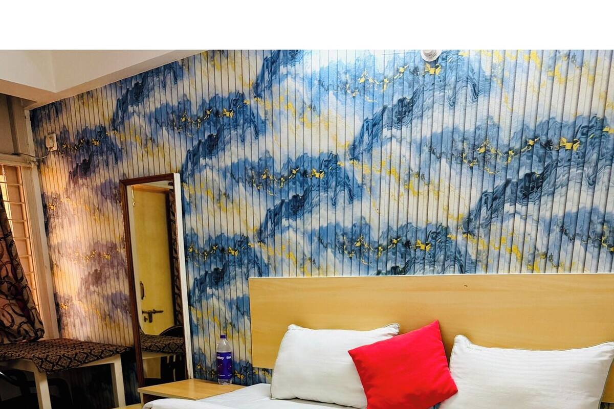 Une chambre d’hôtel avec un grand lit, une tête de lit en bois, un miroir et un mur orné d’un motif abstrait aux couleurs bleue et jaune.