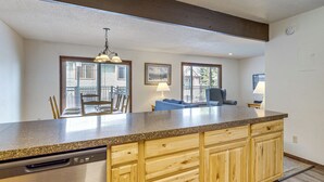 A kitchen with a granite countertop, wooden cabinets, a dishwasher, and a dining area with a table and chairs. - Hot Tub! Walkable Condo 3 Mi to Winter Park Resort (Winter Park)