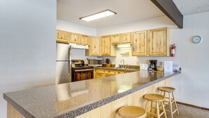 A kitchen with wooden cabinets, a granite countertop, a stainless steel refrigerator, a microwave, and a coffee maker. - Hot Tub! Walkable Condo 3 Mi to Winter Park Resort (Winter Park)