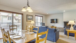 A dining area with a wooden table set for four, a blue patterned sofa, a television, and a fireplace. - Hot Tub! Walkable Condo 3 Mi to Winter Park Resort (Winter Park)