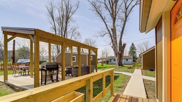 Eine Holzterrasse mit Grillplatz, ein Betonweg und ein Haus im Hintergrund.