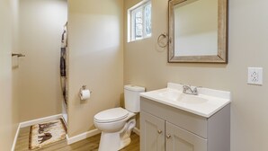 Ein Badezimmer mit Toilette, Waschbecken, Spiegel und einem kleinen Fenster.