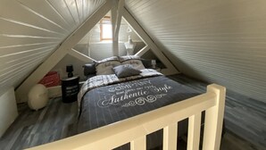 Un dormitorio tipo loft con techo inclinado, una cama con colcha estampada oscura y un ventanal con vistas al exterior.