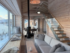 Interior moderno de una cabaña de troncos con sofá, comedor y escalera.