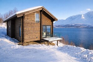 A wooden cabin with a glass balcony overlooking a lake and mountains.