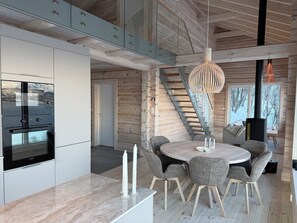 A modern kitchen with a built-in oven, a dining area with a round table and chairs, and a staircase leading to a loft.