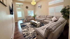 Ein Wohnzimmer mit einem Ecksofa, einem Couchtisch, einer Chandelüster und einer großen Pflanze.