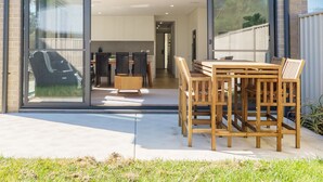 A modern house with a patio, a dining area, and a garage visible through the glass doors.