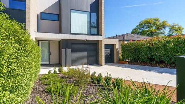 A modern two-story house with a garage, large windows, and a well-maintained garden.