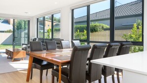 A modern dining area with a wooden table, black chairs, and large windows offering views of a residential neighborhood.