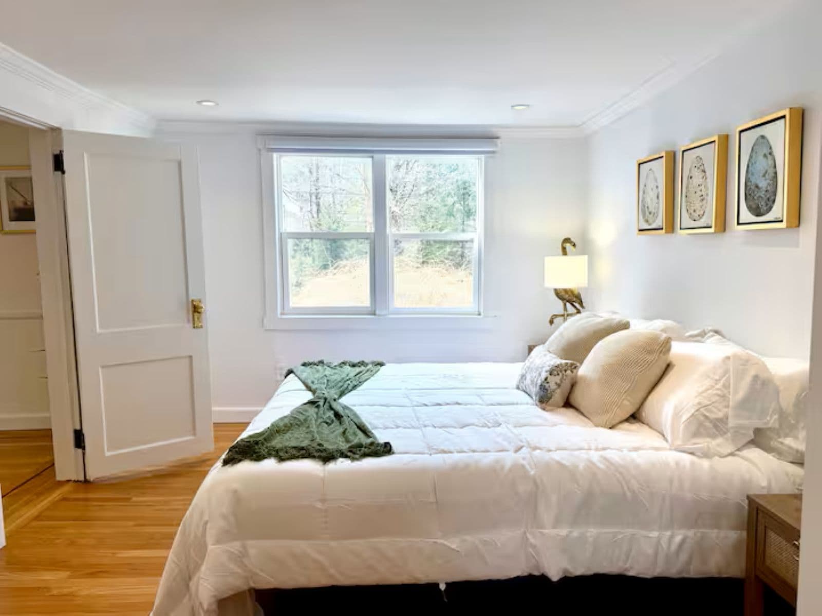 A bedroom with a large bed, a window, and framed artwork on the wall.