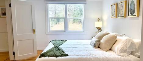 A bedroom with a large bed, a window, and framed artwork on the wall.